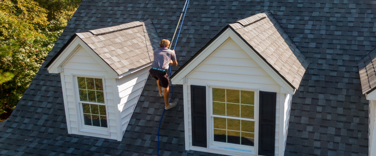 Man on the roof of a house inspecting a black tile roof.